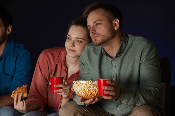 Muotokuva aikuisten pari katsomassa elokuvia kotona syödessään välipaloja ja popcornia istuu sohvalla pimeässä huoneessa
 - Valokuva, kuva