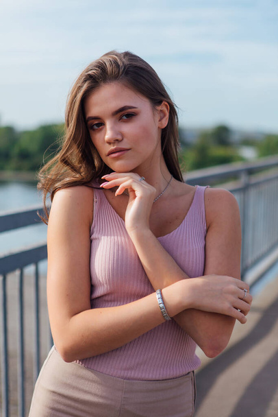 Close up warm summer portrait of a young beautiful woman posing on the old rusty transport bridge over the river during sunset. - Zdjęcie, obraz