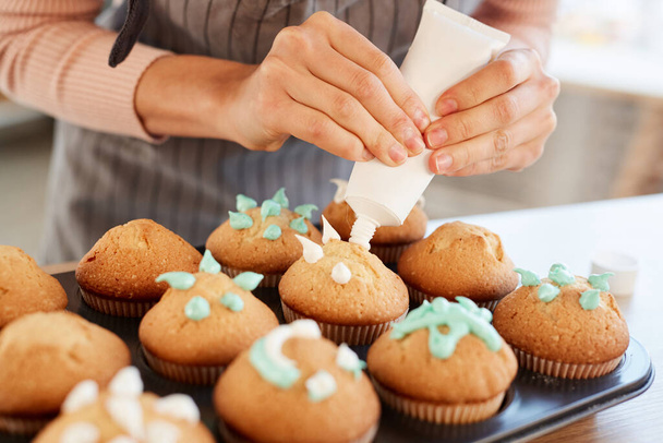 Tunnistamaton leipuri seisoo koristelu tuoreita kotitekoisia cupcakes makea kerma, vaakasuora lähikuva laukaus
 - Valokuva, kuva
