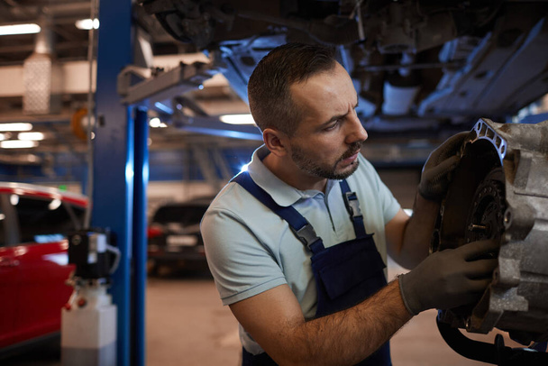 Porträt eines bärtigen Automechanikers, der in der Autowerkstatt ein Getriebe repariert, Kopierraum - Foto, Bild