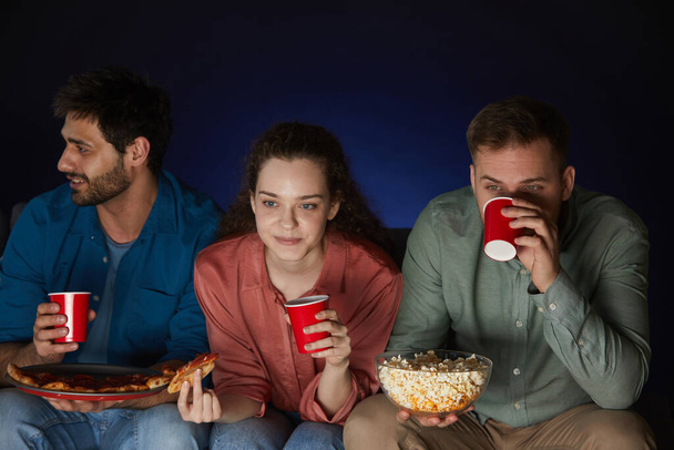 Groupe d'amis regardant des films à la maison tout en mangeant des collations et du pop-corn assis sur un grand canapé dans une pièce sombre, copiez l'espace ci-dessus
 - Photo, image