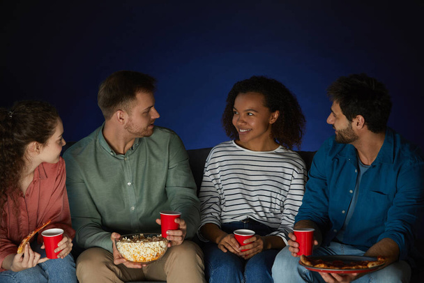 Mnohonárodnostní skupina lidí, kteří drží misku popcornu, zatímco diskutují o filmu v tmavé místnosti doma, kopírovací prostor - Fotografie, Obrázek