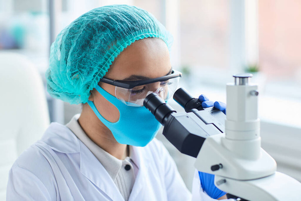 Widok z boku portret kobiety naukowiec patrząc w mikroskop podczas pracy nad badaniami w laboratorium medycznym, przestrzeń kopiowania - Zdjęcie, obraz