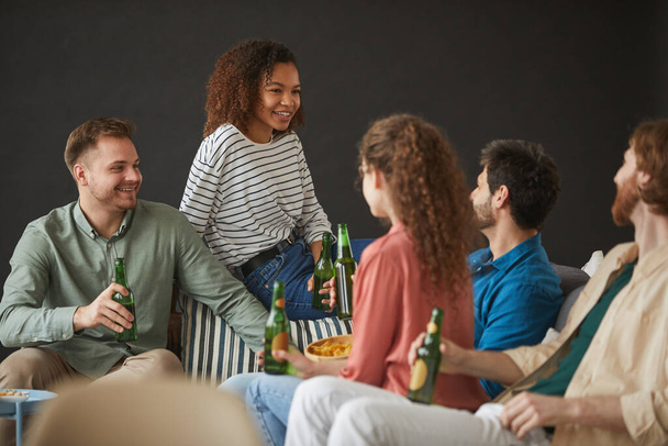 Nagy baráti társaság élvezi a sört és snackeket a hazai party fekete háttér, másolás tér - Fotó, kép