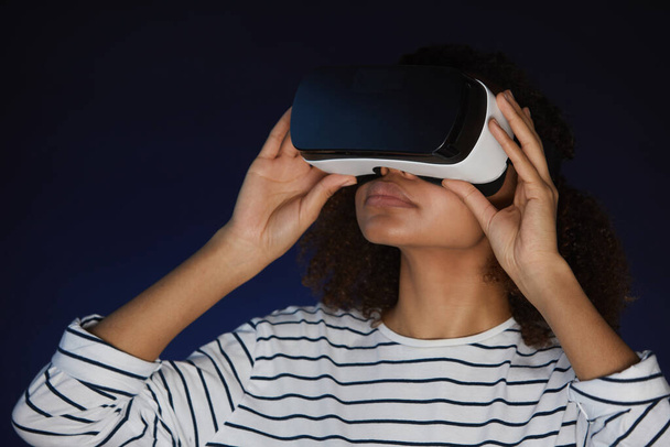 Head and shoulders portrait of mixed-race young woman wearing virtual reality gear while enjoying immersive videogame or movie in dark - Photo, image