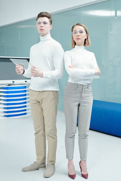 Młodzi eleganccy menedżerowie futurystycznego biura technologii lub ośrodka w inteligentnych okularach stojący naprzeciw interaktywnego wyświetlacza i informacji skanujących - Zdjęcie, obraz