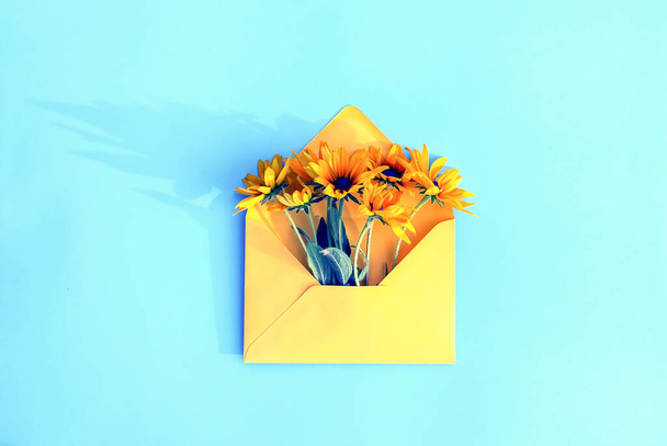 Yellow paper envelope with garden rudbeckia flowers on light blue background. Festive floral template. Greeting card design. Top view. Vintage style. Black-eyed susan plant. - Fotografie, Obrázek