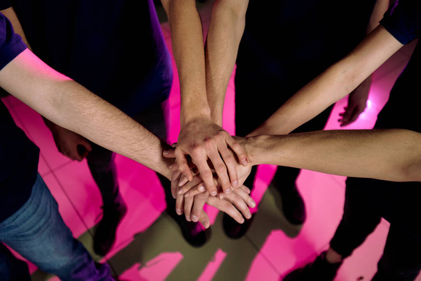 Над видом неузнаваемых людей, стоящих в кругу и складывающих руки как символ командной работы
 - Фото, изображение