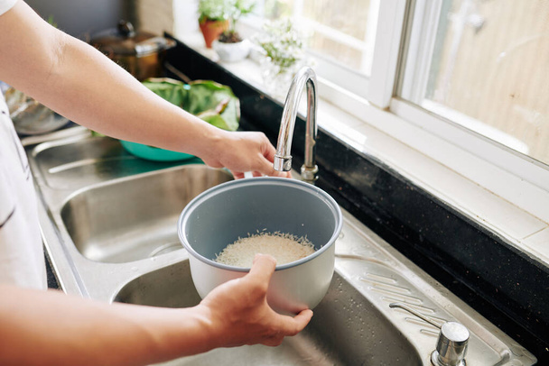Nő öblítő tál rizs alatt csapvíz a konyhában, amikor főzés vacsora otthon - Fotó, kép
