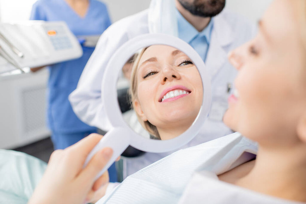 Refleksja w lustrze zdrowego uśmiechu pięknej młodej uśmiechniętej pacjentki klinik stomatologicznych po zabiegu wybielania zębów przez dentystę - Zdjęcie, obraz