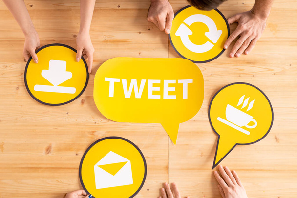 Над просмотром маркетологи обсуждают идеи для твитов на мозговом штурме, желтые иконки на деревянном столе
 - Фото, изображение