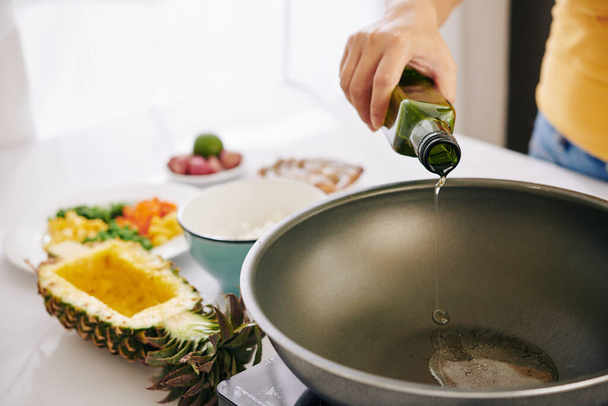 Жінка наливає рослинну олію на сковороду, щоб обсмажити рис з овочами і зробити традиційну страву
 - Фото, зображення