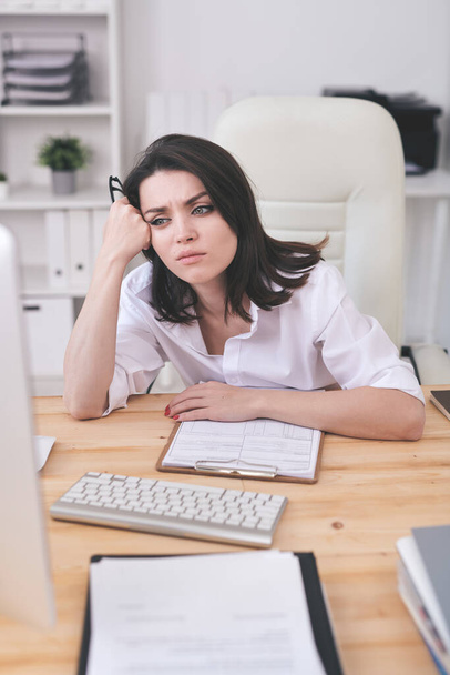 Молода втомлена або роздратована бізнес-леді сидить за столом перед екраном комп'ютера, чекаючи вивантаження онлайн-сторінки
 - Фото, зображення