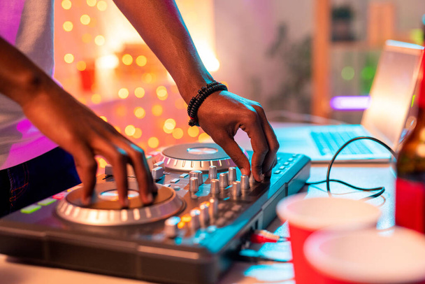 Handen van de jonge Afrikaanse man bewegen draaitafel en draaien schakelaar terwijl het mengen van geluiden om dansmuziek te maken op het feest in de nachtclub - Foto, afbeelding