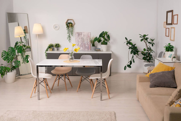 Interior de acogedora sala de estar con mesa de comedor, sofá verde macetas plantas y marcos en las paredes
 - Foto, imagen