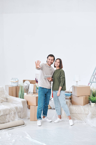 Cheerful young couple in casualwear discussing where to put new furniture or tv set while standing in the center of living-room - Foto, imagen
