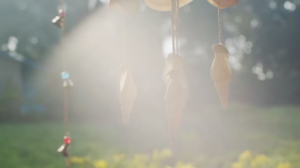 Marine wind chime made of seashells hanging outdoors backlit with sun rays lens flare. Tropical decoration spinning sunlit in summer sunlight slow motion. atmospheric wallpaper boho-chic style design - Footage, Video