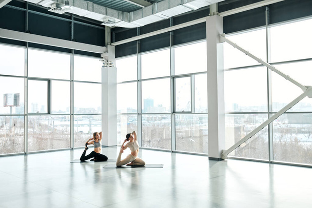 Дві активні жінки вправляються на килимках з руками за головами під час тренувань з фітнесу у великому сучасному центрі відпочинку
 - Фото, зображення