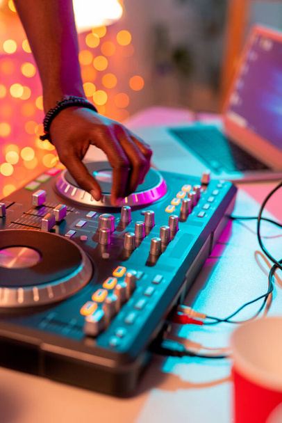 Hand eines jungen männlichen DJs afrikanischer Herkunft über Plattenteller, der beim Mischen von Sounds in der Disco oder auf einer Heimparty für zusätzliche Lautstärke sorgt - Foto, Bild