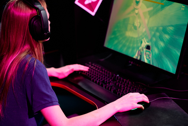 Młoda kobieta w słuchawkach zaangażowana w grę wideo w gry wideo online w klubie sportowym cybernetycznym - Zdjęcie, obraz