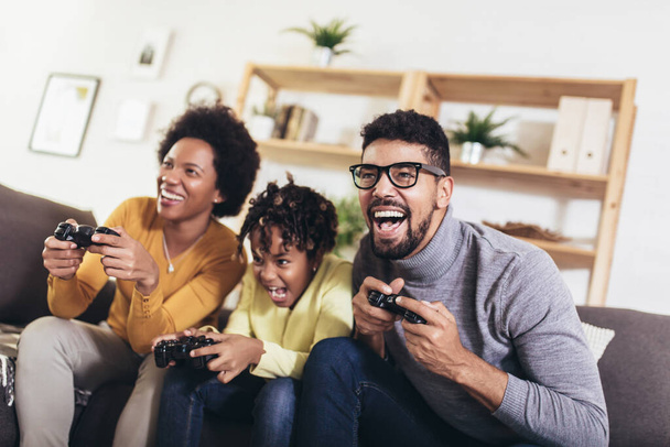 Афроамериканская семья сидит дома на диване и вместе играет в видеоигры
 - Фото, изображение