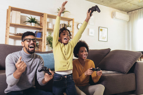 Famille afro-américaine à la maison assise dans un canapé et jouant ensemble à des jeux vidéo sur console
 - Photo, image