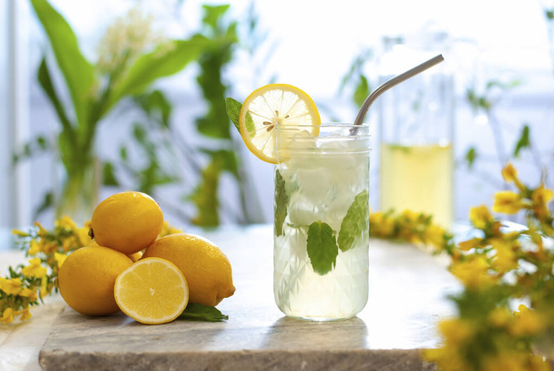 Citrus iced lemonade in pitcher and glasses with lemon slice and mint leaves decoration and on marble table on natural background. Fresh summer drink beautiful picture. Copy space - Фото, зображення