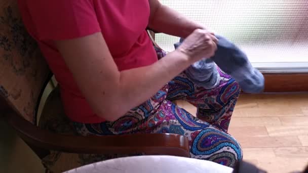 Μεγαλύτερη κυρία που κάθεται σε μια καρέκλα διπλώνοντας κάλτσες στο σπίτι - Πλάνα, βίντεο
