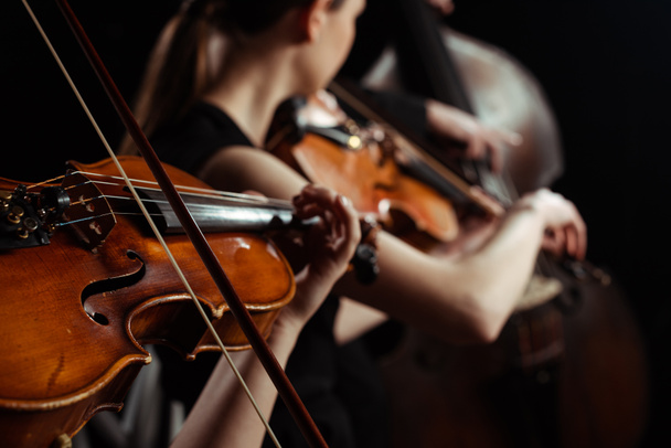 cropped view of female professional musicians playing on violins on dark stage, selective focus - Foto, Imagem