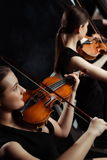 young professional musicians playing classical music on violins on dark stage  - Photo, Image
