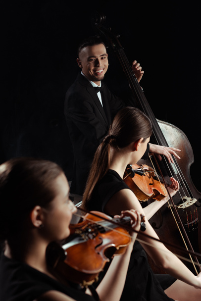 szczęśliwi profesjonalni muzycy grający na kontrabasie i skrzypcach wyizolowanych na czarno - Zdjęcie, obraz