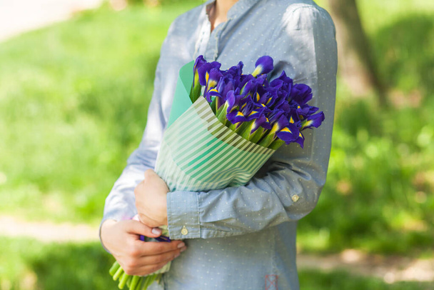 Chica sostiene un ramo con iris, sobre un fondo de hierba verde. primer plano
 - Foto, Imagen