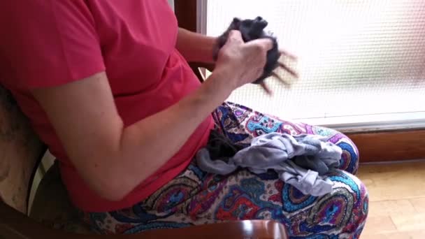 Vanhempi nainen istuu tuolissa viikkaamassa sukkia kotona
 - Materiaali, video
