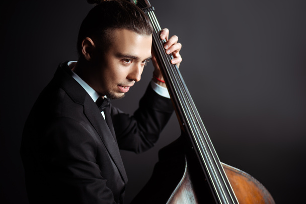 young professional musician playing on double bass on dark stage - Photo, Image