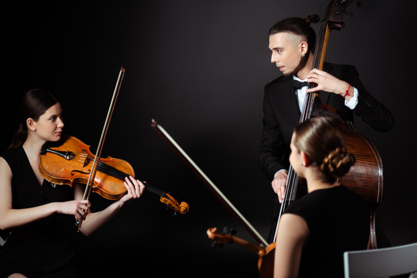 Trio professioneller Musiker auf Musikinstrumenten auf dunkler Bühne - Foto, Bild