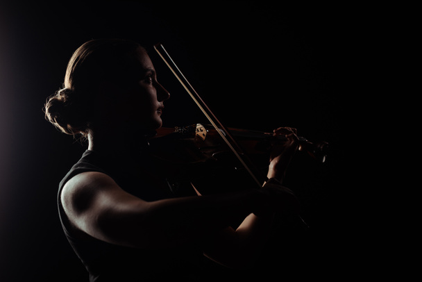 silhouette of female musician playing on violin on dark stage - Zdjęcie, obraz