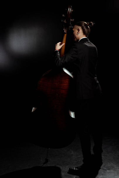 Задний вид профессионального музыканта, играющего на бас-гитаре на темной сцене
 - Фото, изображение