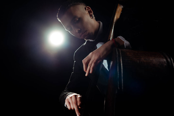músico profissional tocando no contrabaixo no palco escuro com luz de volta
 - Foto, Imagem