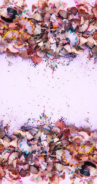 Wooden pencil shavings and colorful crumbs of graphite from sharpener on soft pink paper background. Top view. Symmetrical design with empty space for text for poster, banner, cards. - Photo, image
