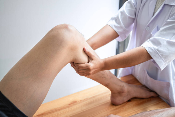 Lékař nebo fyzioterapeut pracující vyšetřuje léčbu poraněné nohy atletického pacienta, Dělat rehabilitační terapie bolest na klinice. - Fotografie, Obrázek