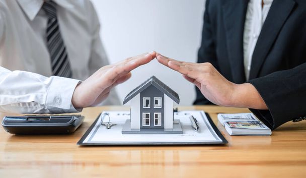 Agent nieruchomości i klient obejmujące Model małego domu i ochrony przez ręce. - Zdjęcie, obraz