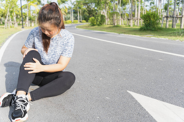 Азиатка использует руки держать ее травму колена во время пробежки по дороге в парке, Травма от концепции тренировки
. - Фото, изображение