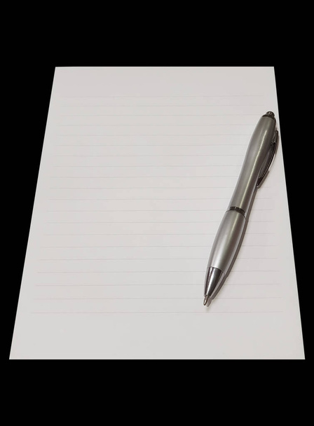 Close-up of a notepad. Gray silver ballpoint pen on the sheet. Notepad with lines. Isolated on black background. Top view of blank note paper with pen. Copy space. School and education concept. - Photo, Image