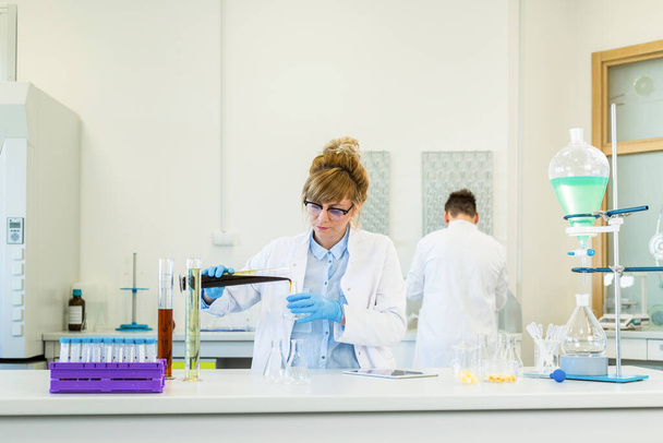女性化学者は実験室で麻CBDとCBDaの油で働いています。彼女はラテックス手袋、ガラス管とエルレンマイヤーフラスコを使用しています。大麻の種からの医療薬局. - 写真・画像