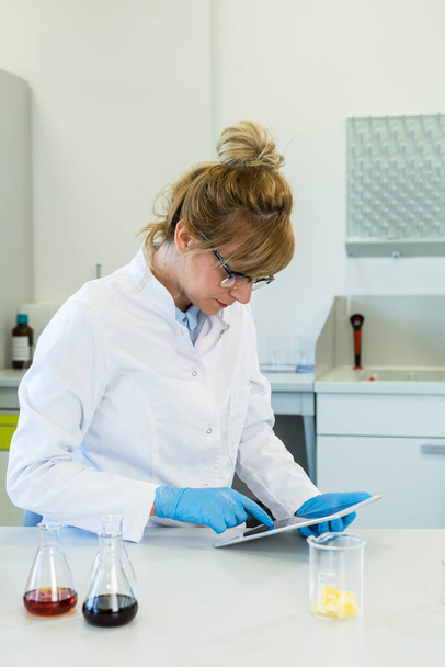 Vrouwelijke chemische wetenschapper houdt vinger over vinger blanco tablet scherm in het laboratorium. Marihuanaknop, CBD en CBDa oliën liggen op tafel. Gezondheidszorg apotheek van cannabis zaden. - Foto, afbeelding