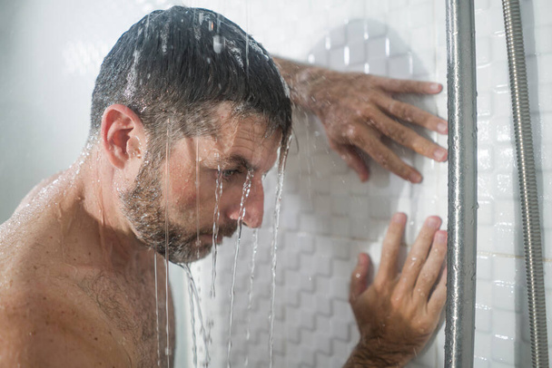 home bathroom dramatic portrait of young attractive sad and depressed man in the shower leaning against the wall thoughtful feeling overwhelmed by life problem  - Foto, afbeelding