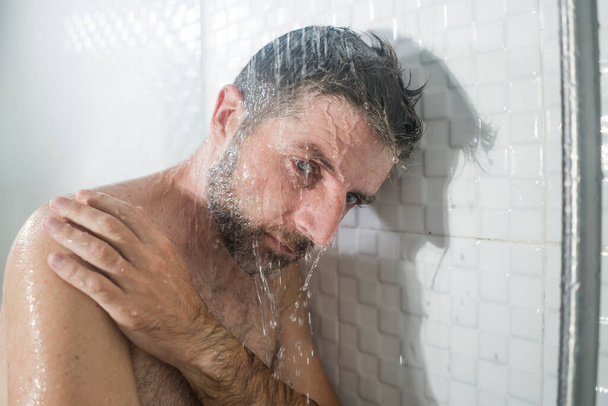 home bathroom dramatic portrait of young attractive sad and depressed man in the shower leaning against the wall thoughtful feeling overwhelmed by life problem  - Photo, image