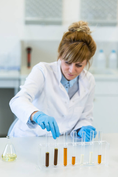 ガラスを身に着けている女性化学者は実験室で麻CBDおよびCBDaオイルと働く。彼女はラテックス手袋、ガラス管とエルレンマイヤーフラスコを使用しています。大麻の種からの医療薬局. - 写真・画像