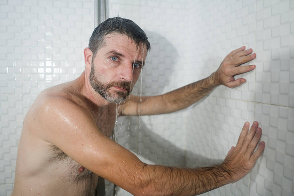 home bathroom dramatic portrait of young attractive sad and depressed man in the shower leaning against the wall thoughtful feeling overwhelmed by life problem  - Foto, Imagen