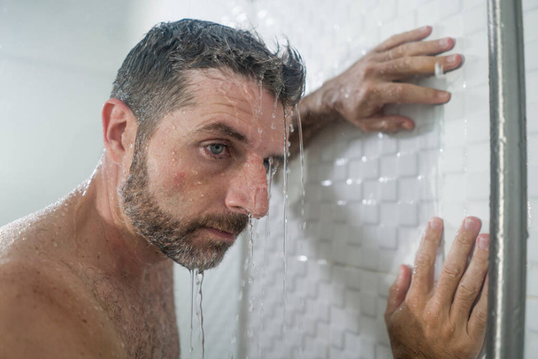 home bathroom dramatic portrait of young attractive sad and depressed man in the shower leaning against the wall thoughtful feeling overwhelmed by life problem  - Fotografie, Obrázek